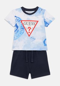 T-shirt à manches courtes bleu tie-dye avec un logo triangle rouge et un short noir doté d'une ceinture élastique et d'un cordon de serrage.