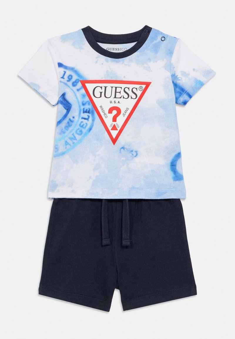 T-shirt à manches courtes bleu tie-dye avec un logo triangle rouge et un short noir doté d'une ceinture élastique et d'un cordon de serrage.