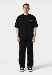 Sort bomulds T-shirt med korte ærmer og hvid grafisk tekst. Sammen med sorte bukser med cremede sidelister og sorte sneakers.