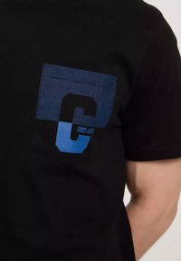 Czarny t-shirt z niebiesk ą paskowaną kieszenią, na której znajduje się duża niebieska litera "C" oraz napis "CROSS JEANS DENIM FOR LIFE". Krótkie rękawy, okrągły dekolt.
