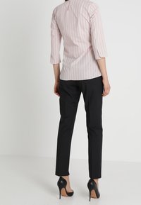 Blouse rose clair à rayures verticales avec manches trois-quarts et ouverture en forme de goutte au dos. Associée à un pantalon noir élégant et des talons hauts.