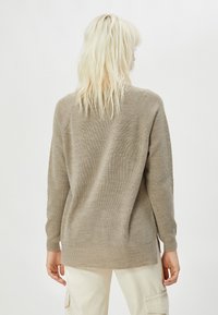 Beige Strickpullover mit strukturiertem Oberflächen, langen Ärmeln und leicht geschwungenem Saum. Die Rückseite hat eine lockere Passform und Raglan-Nähte.
