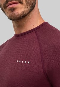 Bordowa sportowa koszulka z teksturowanej tkaniny, okrągłym dekoltem i białym logo "FALKE" na przodzie, z wzmocnionymi szwami.