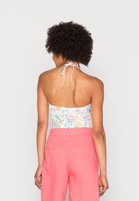 Top halter floral com um fecho branco, combinado com calças de linho rosas de cintura alta, exibindo uma textura suave e cores vibrantes.