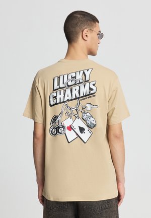T-shirt beige in cotone con una grafica audace sul retro che riporta il testo "LUCKY CHARMS" e vari carte da gioco e dadi.