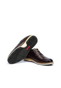 Zapatos de cuero marrón oscuro con una textura suave, que presentan un diseño de cordones, suela clara en contraste y una suela de goma negra con patrón.