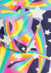 Bunt bedruckter Stoff mit einem Muster aus Regenbogenspiralen und weißen Sternen, der lebendige Farben in Pink, Gelb, Türkis und Lila zeigt.