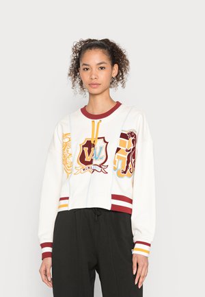White cropped sweatshirt with maroon and yellow striped hem, featuring bold embroidered graphics of animal crests and text details in blue.