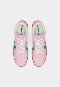 Ζευγάρι ροζ σουέντ αθλητικά παπούτσια Converse με λευκά κορδόνια και πράσινα λογότυπα αστεριού, που φαίνονται από ψηλά σε απλό λευκό φόντο.