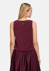 Top senza maniche bordeaux con superficie tessurizzata, caratterizzato da un dettaglio a chiave sul retro e una gonna liscia e fluente.