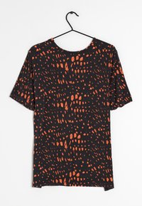 Camiseta negra de manga corta, con un audaz patrón abstracto en naranja y un cuello redondo, colgada de un gancho negro.