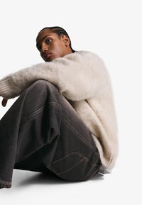 Cremiger, flauschiger Strickpullover, graue Denim-Hose mit weitem Bein und kontrastierenden Nähten. Die weiche Textur des Pullovers kontrastiert mit dem glatten Finish der Jeans.