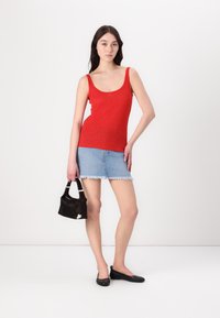 Débardeur rouge, jupe en jean mini avec ourlet effiloché et ballerines noires. Accessoire : petit sac à main noir avec une poignée courte.