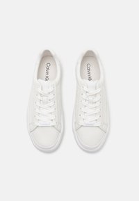 White sneakers with textured sides, lace-up design, and logo on the insole. Features smooth material and a rounded toe. Rubber sole.