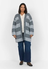 Cardigan rayé gris et gris clair avec une texture douce, doté d'un devant boutonné et d'une coupe décontractée, associé à un jean flare bleu en denim.