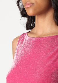 Tettsittende ermeløs topp i levende rosa, med en skimrende tekstur og en glatt halsringning. Stoffet har en reflekterende, metallisk finish.