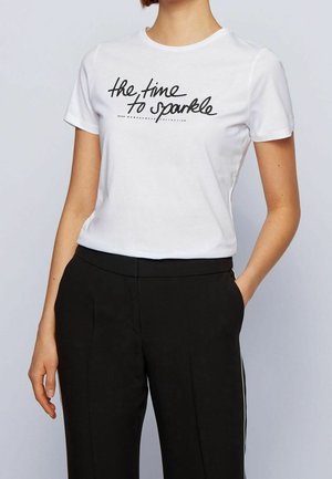 Biała bawełniana koszulka z zaokrąglonym dekoltem i krótkimi rękawami, z czarnym kursywą napisem "czas na błyszczenie".