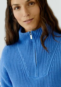 Blauer Strickpullover mit Stehkragen und halbem Reißverschluss. Verfügt über eine gerippte Textur und diagonale Muster auf der Vorderseite.