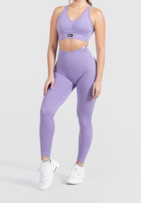 Light purple ribbed sports bra and high-waisted leggings set, featuring a v-neckline and seamless design. Paired with white athletic sneakers.