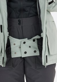 Ljusgrå ytterjacka med ett svart innerlager, som har en åtsittande midja och tryckknapps-stängning. Strukturerad tyg med en geometrisk design.