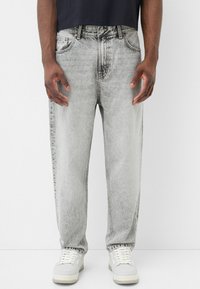 Ljust grå, urblekta jeans i rak passform. Har fem fickor, synliga sömmar och knappgylf.