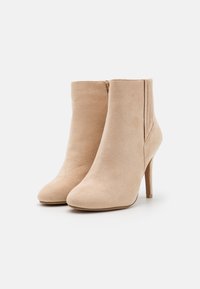 Bottines beiges en daim avec bouts pointus et talons stilettos. Fermeture éclair latérale et détails de couture sur les côtés extérieurs. Surface lisse et texturée.