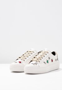 Bílé kožené tenisky se zlatými tkaničkami. Mají vzory hmyzu v červené, zelené a černé barvě. Texturovaná bílá podešev. Hladká podšívka.