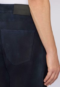 Marineblauwe broeken met een gestructureerde afwerking, voorzien van een achterzak en een leren TRUSSARDI-label bij de taille.