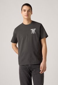 Dark gray cotton t-shirt with short sleeves, featuring a white graphic print reading "GOOD LUCK" and decorative elements on the chest.