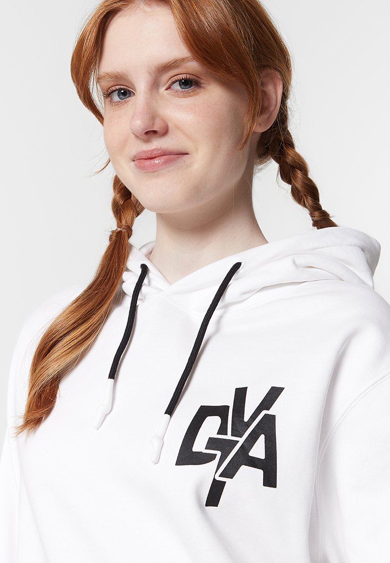 Weißer Kapuzenpullover mit schwarzen Kordeln und einem großen schwarzen Logo auf der linken Brust. Weicher Stoff, entspannte Passform und schlichtes Design.