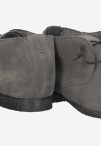 Chaussures en suede gris avec un design à profil bas, texture rugueuse, bords arrondis et une fine semelle en caoutchouc noir. Marque discrète sur le côté.