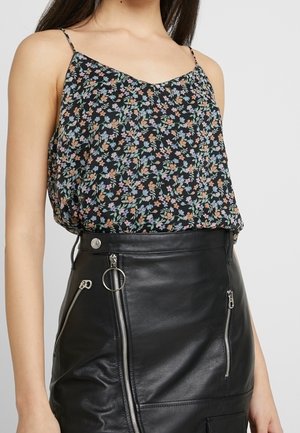 Blouse à fleurs noire avec motifs colorés, fines bretelles et coupe décontractée, associée à une jupe en cuir noire ajustée avec des fermetures éclair et des accents.