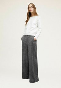 Witte pailletten trui met geribbelde zoom, gecombineerd met hoge taille grijze corduroy wijde broek met zijzakken en verticale strepen.