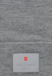 Szary tekstylny materiał dzianinowy z naszywką z logo "PRÓCHNIK" w srebrnych i czerwonych akcentach, wskazującą markę i rok założenia, 1948.