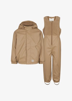 Giacca impermeabile beige con cappuccio e chiusura a scatto, abbinata a salopette senza maniche beige con zip frontale e vita elastica.