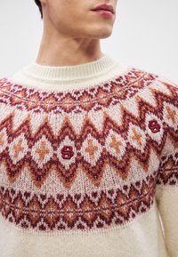Strickpullover in Creme mit einem mehrfarbigen geometrischen Muster in Orange und Burgunderrot. Verfügt über einen runden Ausschnitt und kleine gestickte Akzente.