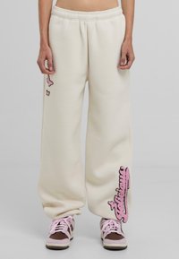 Crème-kleurige wide-leg sweatpants met roze geborduurde accenten van vlinders en tekst, voorzien van een elastische tailleband.