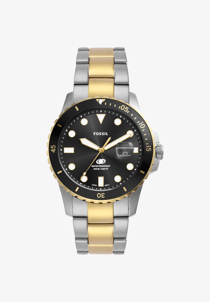 Montre analogique Fossil avec cadran noir, bracelet métal or et argent, index lumineux, lunette tournante et loupe date à 3 heures.
