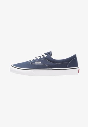 Granatowe płócienne sneakersy z białymi sznurowadłami i przeszyciami, gumowa podeszwa i czarne akcenty. Zawierają metkę z logo Vans po boku.