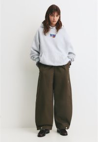 Szara, oversize'owa bluza z kapturem z grafiką "Too Sweet", w połączeniu z luźnymi brązowymi spodniami cargo z zamkami bocznymi i swobodnym krojem. Czarne buty.