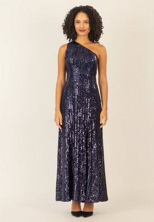 Ein einseitig tragbares, bodenlanges Kleid in dunklem Marineblau mit Pailletten, das einen taillierten Oberteil und einen fließenden Rock mit einem hohen Schlitz bietet. Dazu werden schwarze High Heels getragen.