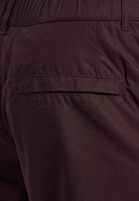 Dunkelbraune Stoffhose mit einem elastischen Bund und einer einzelnen Gesäßtasche mit Klappenverschluss.