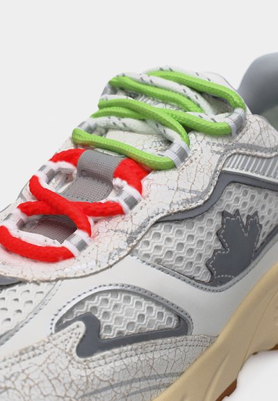 Baskets blanches texturées avec des détails craquelés, des lacets verts et rouges, des panneaux en mesh gris, et un logo feuille d'érable gris sur le côté.