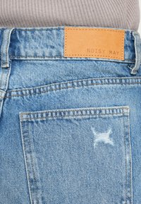 Ανοιχτό μπλε τζιν παντελόνι με καφέ δερμάτινο ταμπελάκι με την επιγραφή "NOISY MAY", με διακριτικά σημάδια φθοράς και τυπικές ραφές.