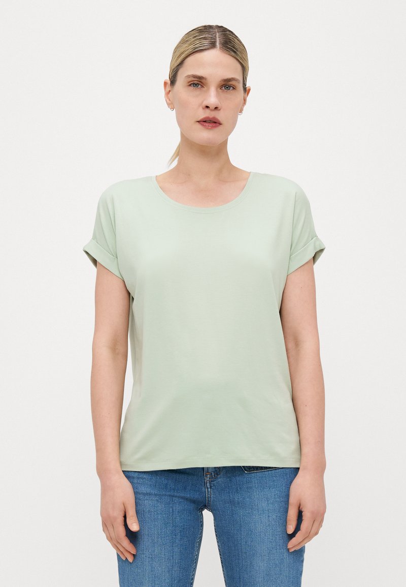 Lys grønn kortermet topp med rund hals og rullet mansjett, laget av mykt materiale; kombinert med blå jeans.