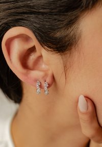 Boucles d'oreilles en argent avec des pierres en zircon cubique scintillantes, présentant un design à trois niveaux et une coupe élégante, suspendues à un crochet simple.