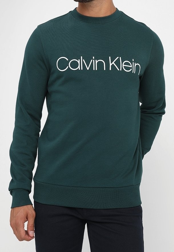 Sudadera verde oscuro con cuello redondo y mangas largas. Presenta un gran logo blanco de "Calvin Klein" en el pecho. Textura suave.