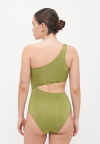 Eén-schouder olive groen badpak met een uitsnijding op de rug en een hooggeknoopte onderkant. Glad, rekbaar stofmateriaal.