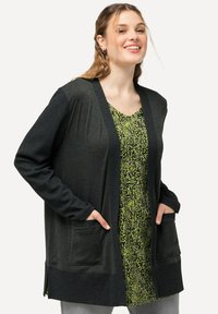 Mörkgrå cardigan i texturerad tyg, med öppen front, två framfickor och ribbade ärmslut. Lager på ett grönt blommigt klänning.
