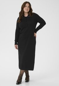 Robe longue noire avec col, manches longues et patte de boutonnage. Fabriquée dans un matériau doux, elle présente une coupe droite et des détails de poignets côtelés.